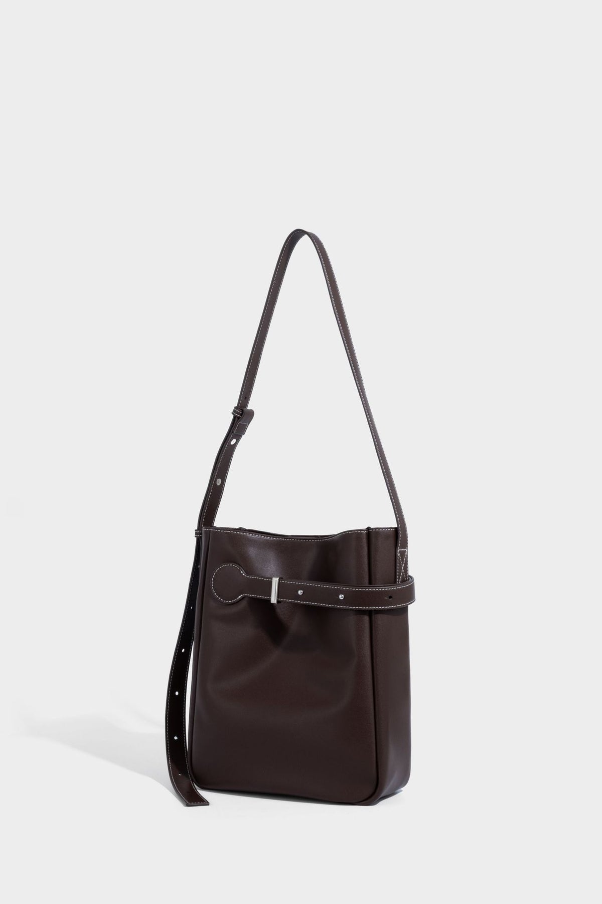 Structured dark brown leather-look bucket bag with white contrast stitching, front wraparound belt buckle strap, and long