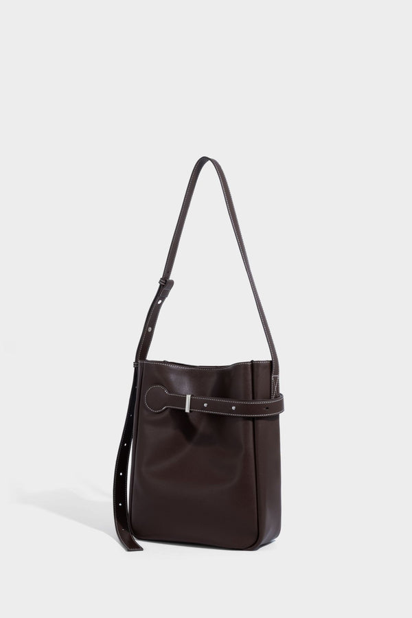 Structured dark brown leather-look bucket bag with white contrast stitching, front wraparound belt buckle strap, and long