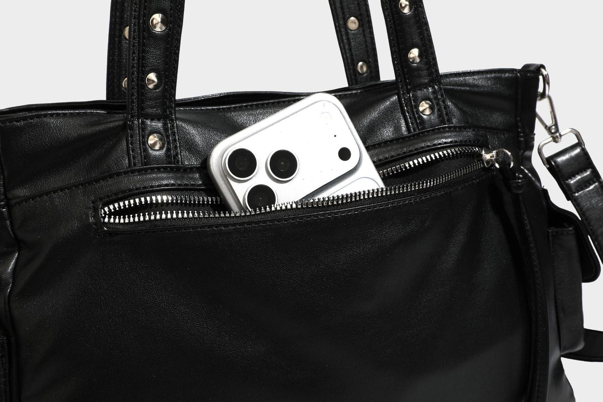 Black leather-look tote bag with silver pyramid studs on handles and front panel, multiple flap and zip exterior pockets