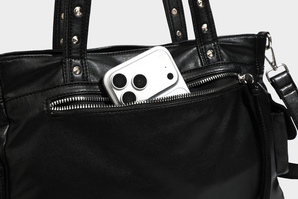 Black leather-look tote bag with silver pyramid studs on handles and front panel, multiple flap and zip exterior pockets