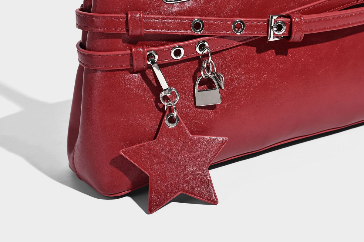 Structured glossy leather-look shoulder bag with wraparound belt straps, silver-tone hardware, and dangling star charm