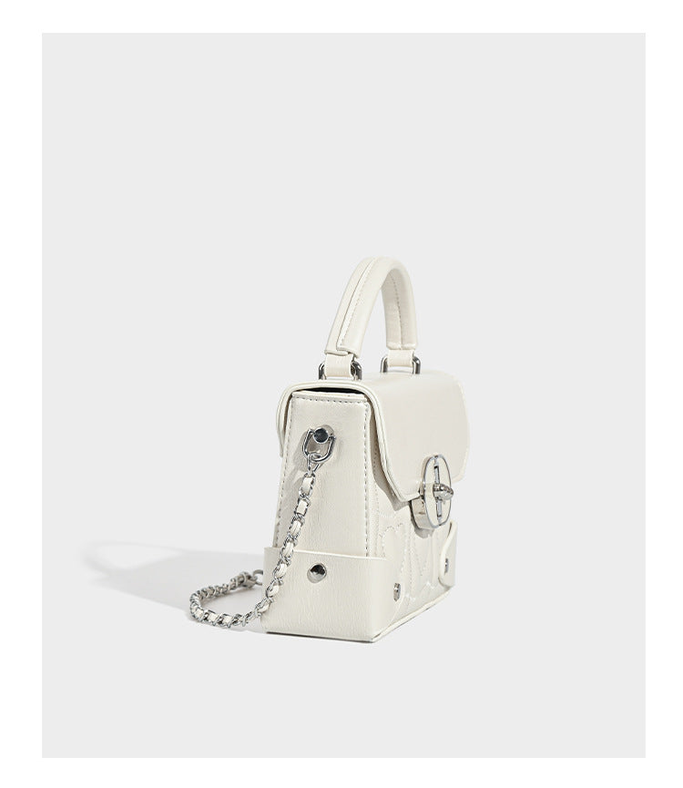 Kleine strukturierte Box-Tasche aus herzförmig gestepptem PU mit Henkel, silberfarbenem Kettenriemen zum Tragen als Crossbody und ovalem Drehverschluss, Detailansicht
