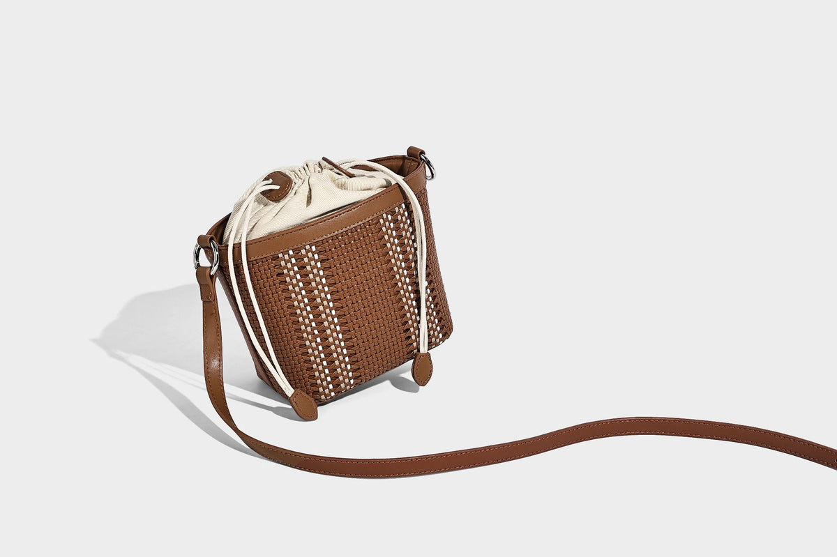 Small woven bucket bag with drawstring top, braided handle, detachable crossbody strap, and silver-tone ring hardware, detail