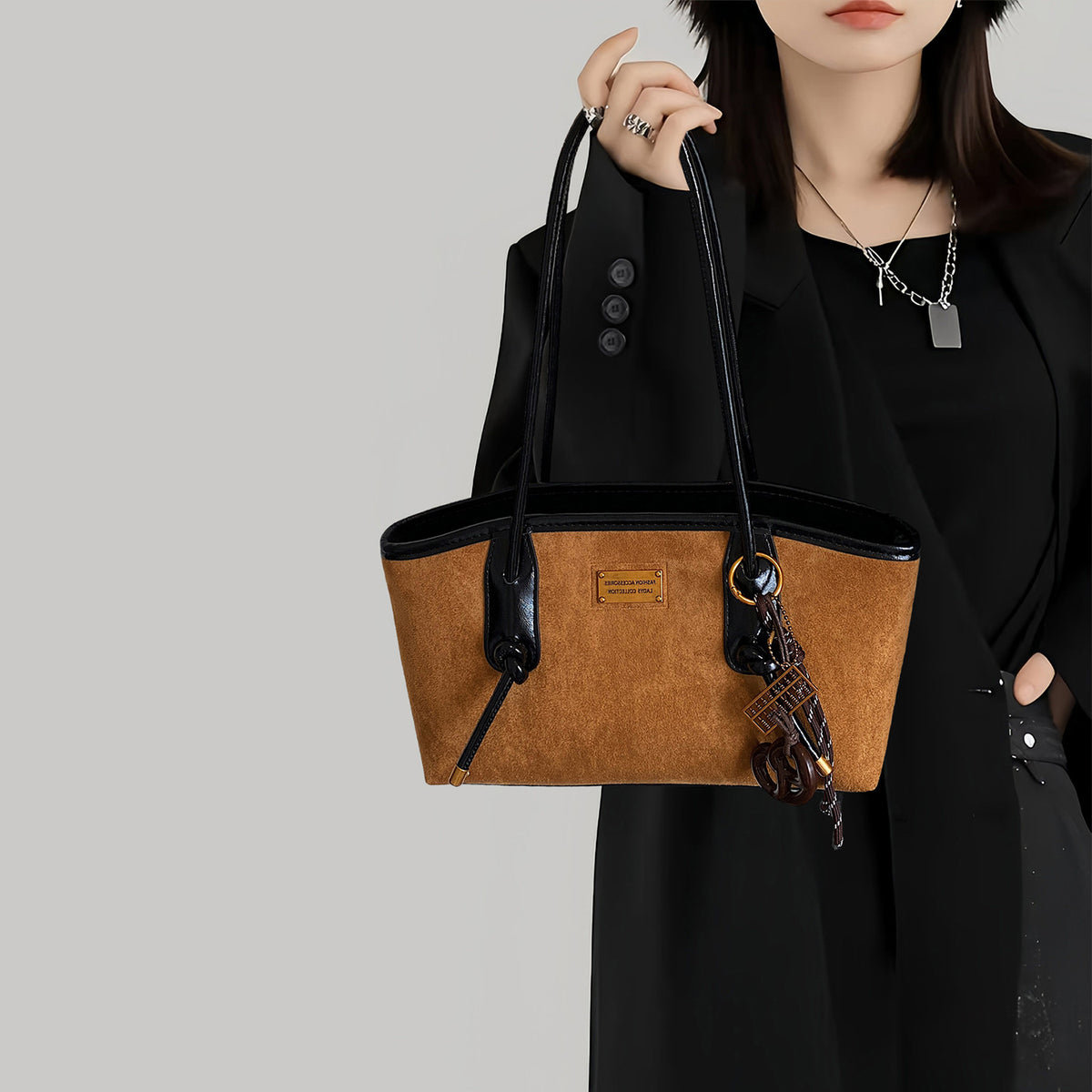 Structured suede-finish tote bag with glossy black leather-look trim, dual top handles, and decorative hanging charm in