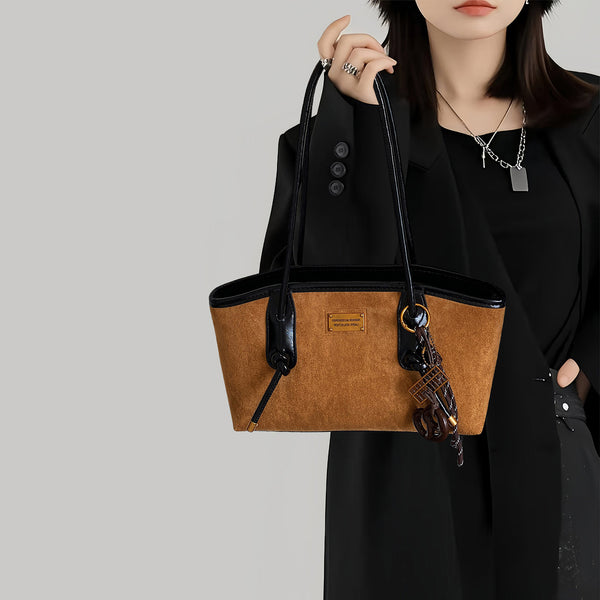Structured suede-finish tote bag with glossy black leather-look trim, dual top handles, and decorative hanging charm in