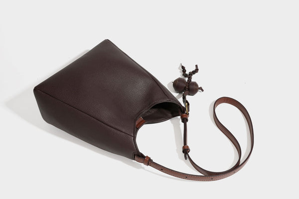 Hobo-Schultertasche in dunklem Espresso mit genarbter Oberfläche, warmen cognacfarbenen Details, verstellbarem schmalem Riemen, goldfarbenen Ringbeschlägen und geknotetem