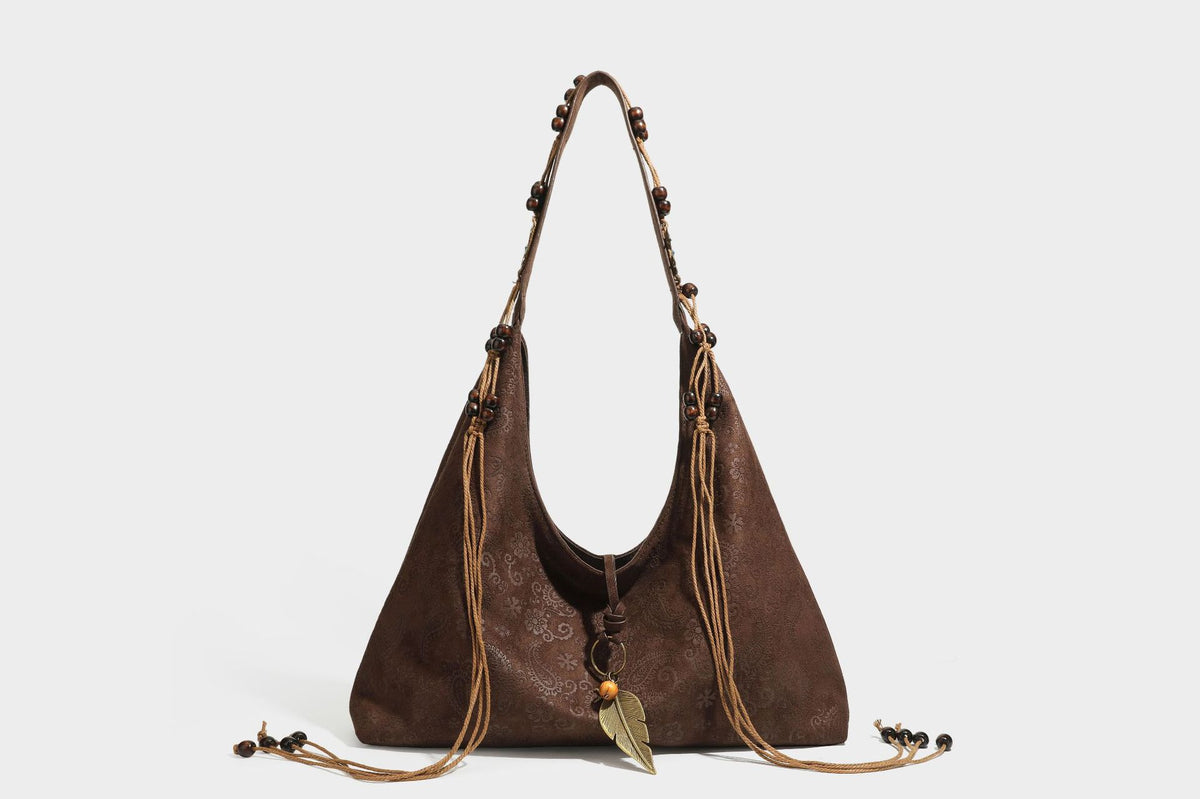 Slouchy boho hobo shoulder bag in embossed brown suede-look finish with beaded strap, cord tassels, and brass-tone leaf