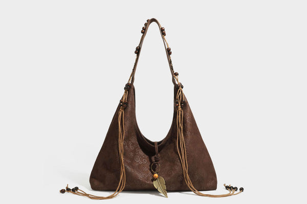 Slouchy boho hobo shoulder bag in embossed brown suede-look finish with beaded strap, cord tassels, and brass-tone leaf