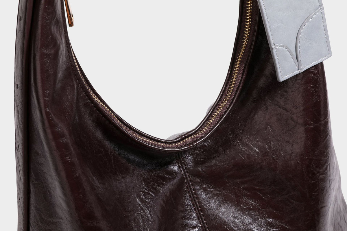 Große dunkelbraune, glänzende, geknautschte Hobo-Schultertasche mit Reißverschluss, goldfarbenen Metalldetails, verstellbarem Trageriemen und Hellblau