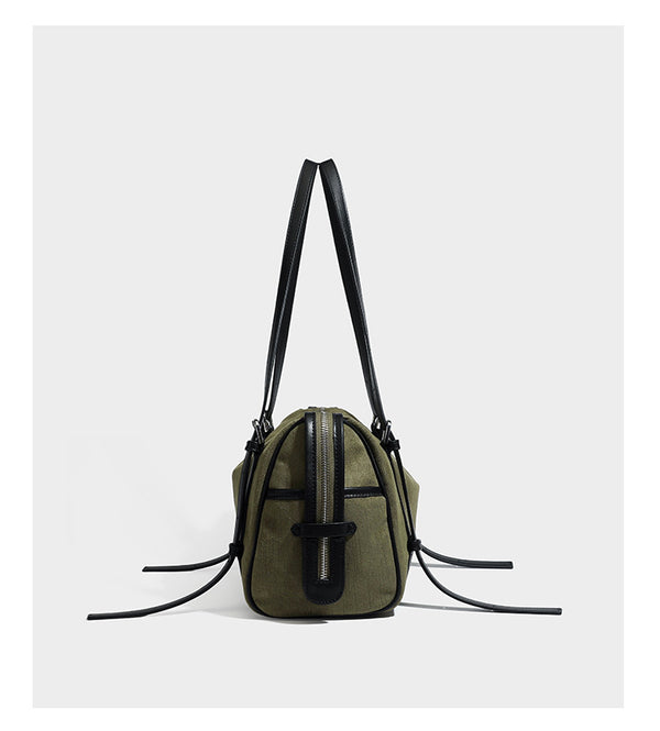 Olivgrüne Schultertasche in Zylinderform aus Canvas mit Riemen in schwarzer Lederoptik, Reißverschluss oben und silberfarbenen Beschlägen, Detailansicht