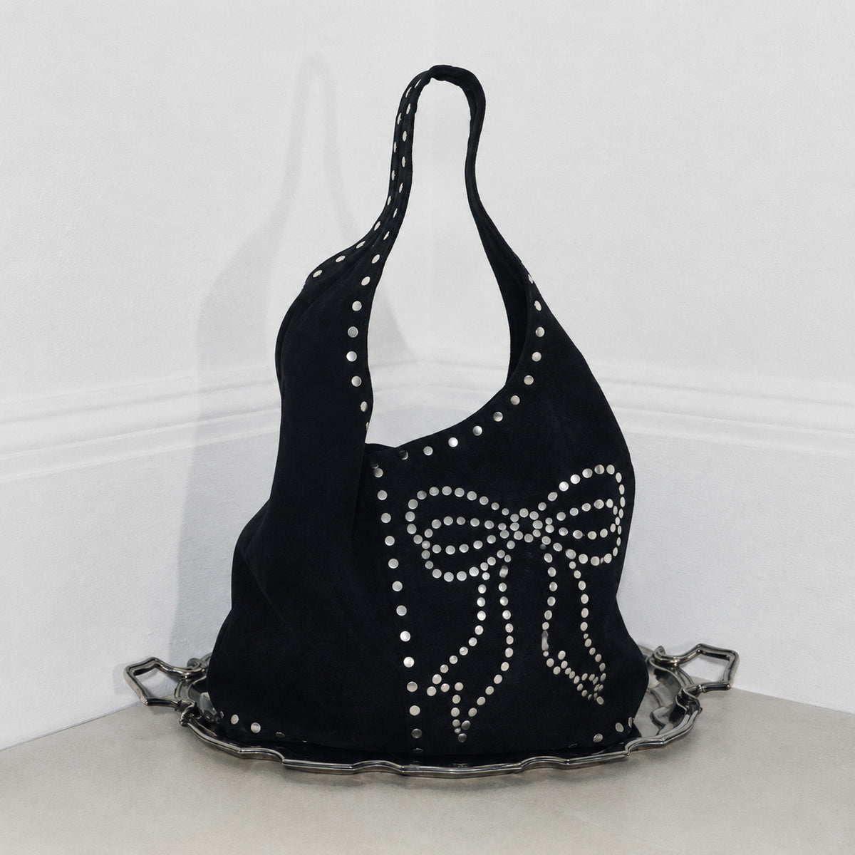 Oversize-Hobo-Schultertasche in schwarzer Velourslederoptik mit silberfarbenen Rundnieten und großem, mit Nieten besetztem Schleifenmotiv auf der Vorderseite, Detailansicht