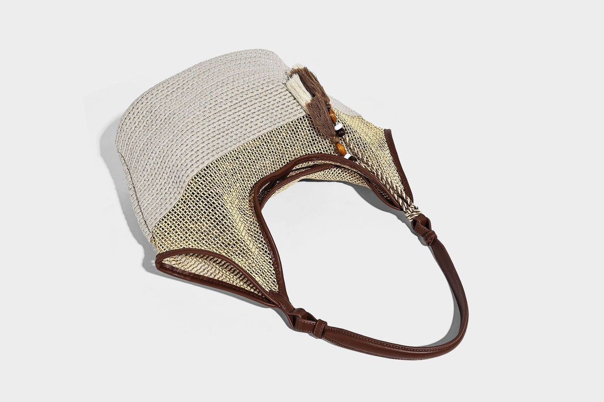 Two-tone beige and cream woven straw hobo shoulder bag with brown leather-look trim, long shoulder strap, and tassel-bead