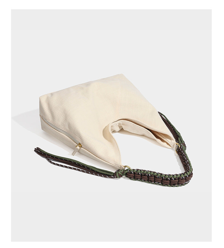 Soft slouchy cream canvas shoulder tote with braided brown and green cord handle, gold-tone ring hardware, and tassel trim