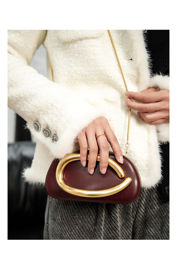 Kleine Crossbody-Clutch in abgerundeter Rechteckform mit übergroßem poliertem C-förmigem Goldhenkel und schmalem Goldkettenriemen, Detailansicht