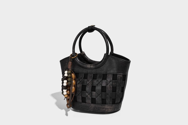 Small woven-panel bucket bag with circular ring handles, beaded tassel charm, and detachable crossbody strap in brown, detail