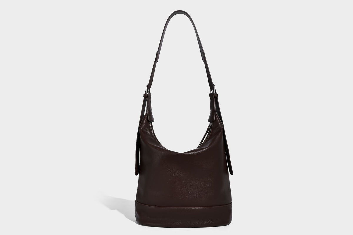Slouchy bucket hobo shoulder bag in dark brown with glossy leather-look finish, top zip closure, and long adjustable, detail
