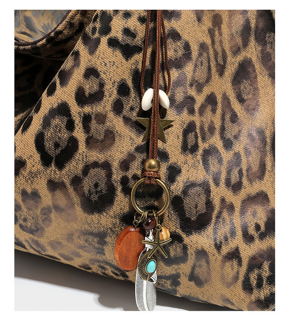 Slouchy leopard print hobo shoulder bag with glossy coated finish, top zipper closure, dark brown trim, and dangling charm