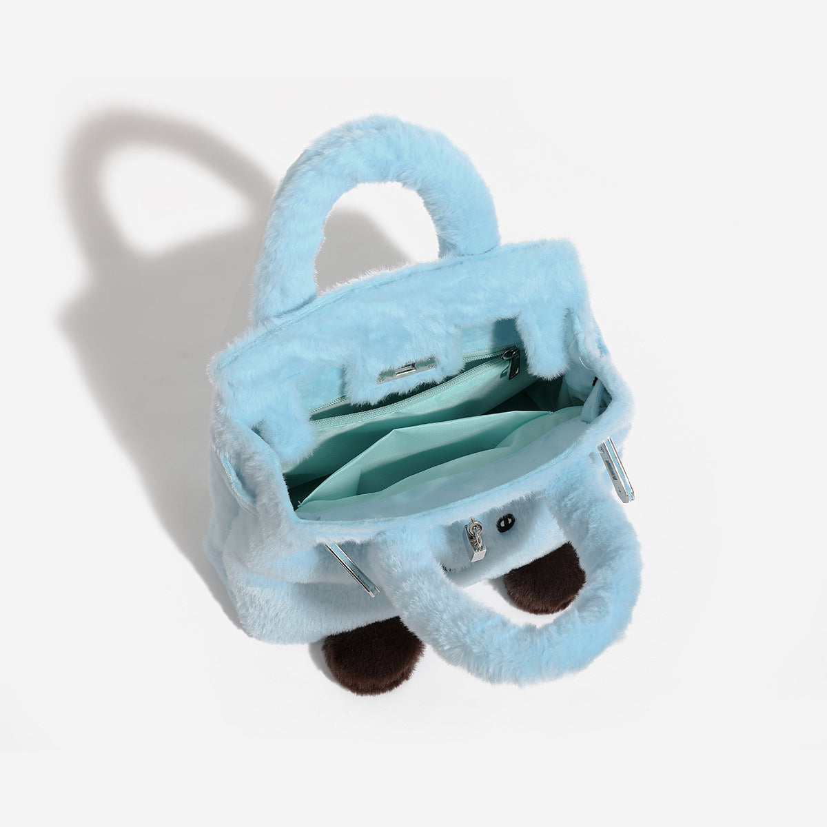 Ice-blue plush faux-fur Kelly-style convertible bag with embroidered smiling face, dark pom-pom feet, silver-tone clasp