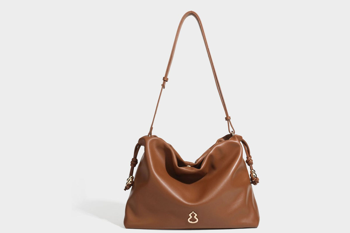 Slouchy ruched drawstring shoulder bag in smooth leather-look finish with gold-tone emblem and slim adjustable strap, detail