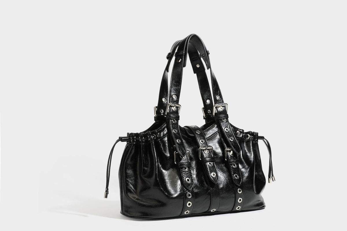 Large black glossy leather-look tote bag with silver buckle straps, eyelet grommet panels, drawstring side gathers, and
