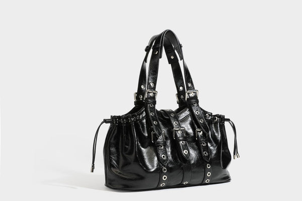 Large black glossy leather-look tote bag with silver buckle straps, eyelet grommet panels, drawstring side gathers, and
