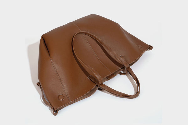 Große, formstabile trapezförmige Tote-Bag aus braunem Lederimitat mit genarbter Oberfläche, zwei Tragegriffen und seitlichen Bindebändern, Detail