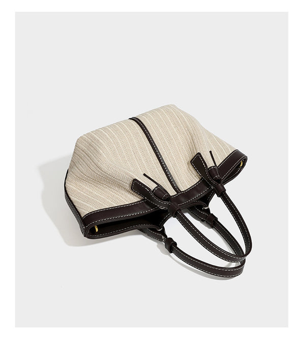 Cremefarbene geflochtene Tote-Bag mit dunkelbraunen Besätzen in Lederoptik, kontrastierenden weißen Nähten, zwei oberen Henkeln und abnehmbarem Schulter