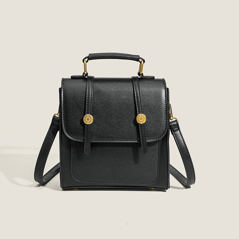 Structured mini satchel backpack with smooth leather-look finish, front flap pocket, gold-tone stud closures, and top handle