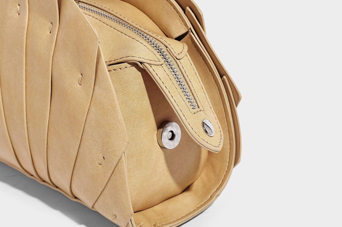 Structured dome satchel with fan-pleated leather-look exterior, dual top handles, and detachable shoulder strap, detail view