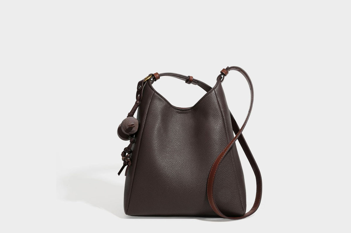 Hobo-Schultertasche in dunklem Espresso mit genarbter Oberfläche, warmen cognacfarbenen Details, verstellbarem schmalem Riemen, goldfarbenen Ringbeschlägen und geknotetem
