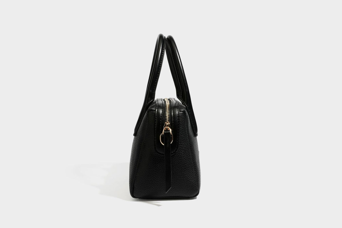 Small structured pillow satchel bag with pebbled leather-look finish, dual rolled top handles, gold-tone gourd emblem, and