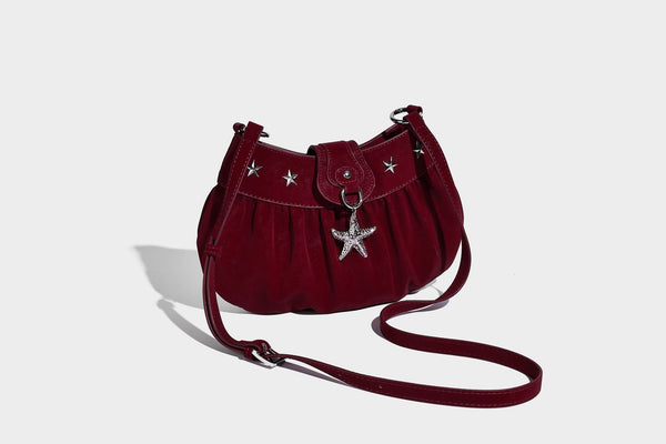 Ruched shoulder bag with curved flap, silver star studs, dangling starfish charm, and adjustable crossbody strap, detail view