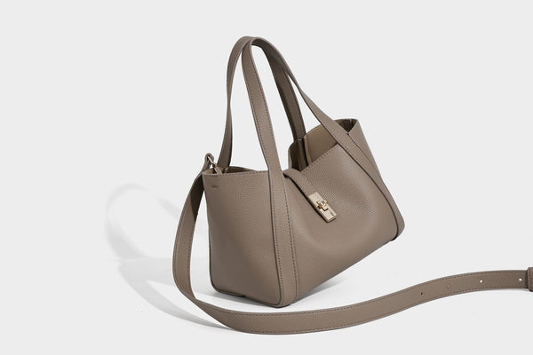 Structured trapezoid tote bag in taupe pebbled leather-look finish with gold-tone turn-lock hardware, dual top handles, and