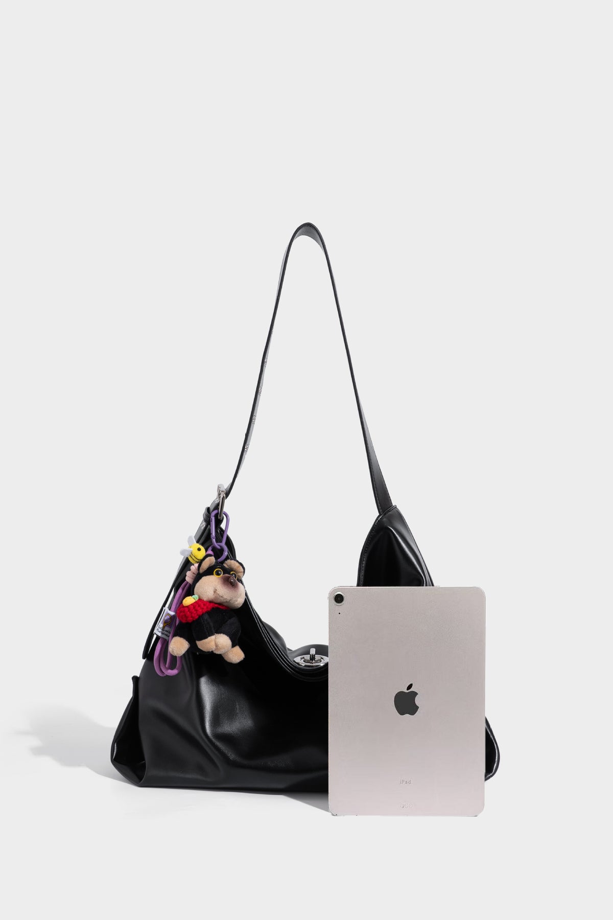 Große schwarze, weich fallende Hobo-Schultertasche in glänzender Lederoptik mit mit Ösen besetztem Riemen, silberfarbenen Metallbeschlägen und abnehmbarem