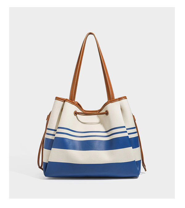 Large cream and navy striped canvas bucket tote bag with tan leather-look trim, drawstring closure, and double shoulder