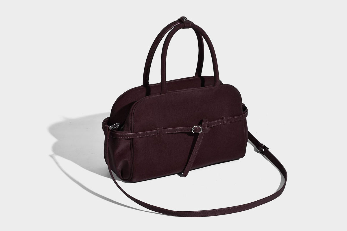 Strukturierte Henkeltasche aus mattem, genarbtem Material mit umlaufendem Riemen und Ringbeschlägen, zwei oberen Tragegriffen und abnehmbarem Crossbody-Riemen