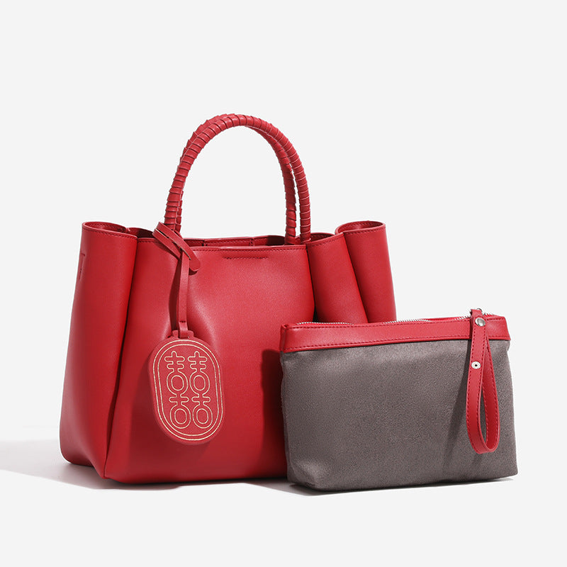 Strukturierte Tote-Bag in mattem Rot mit gedrehten, umwickelten Tragegriffen, Anhänger mit Doppelglück-Symbol und herausnehmbarem grauem Innenfach mit Reißverschluss