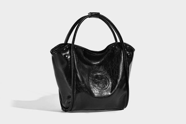 Glossy leather-look structured tote bag with rounded top handles, detachable shoulder strap, embossed front emblem, and side