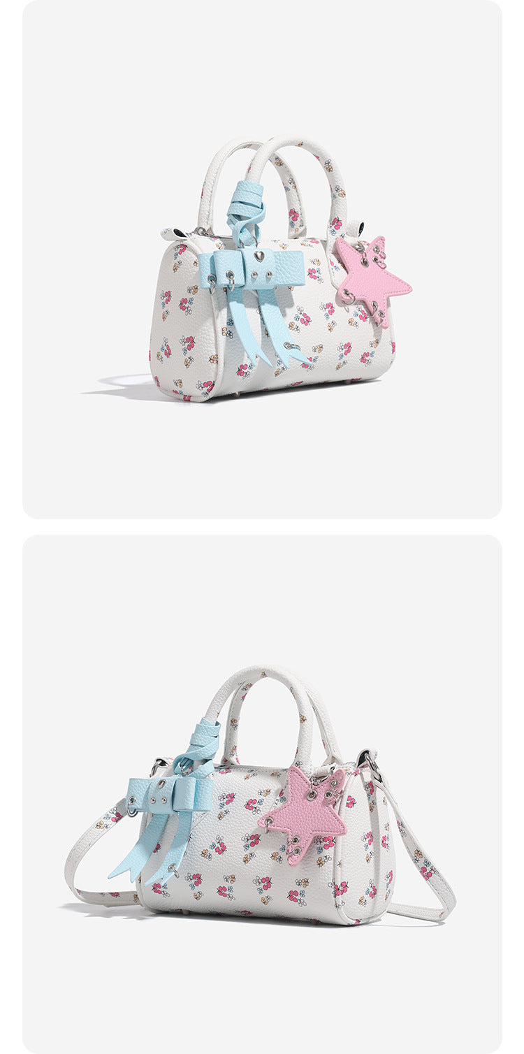 Mini-Boston-Tasche in Weiß mit genarbter Oberfläche, Blumen- oder Kirschprint, pastellblauem Schleifenanhänger, rosafarbenem Sternanhänger und zwei oberen