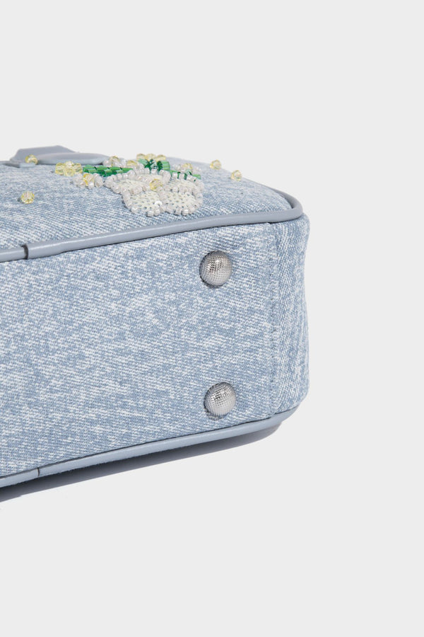 Small light blue denim-look barrel bag with white floral bead embroidery, dual top handles, and detachable shoulder strap