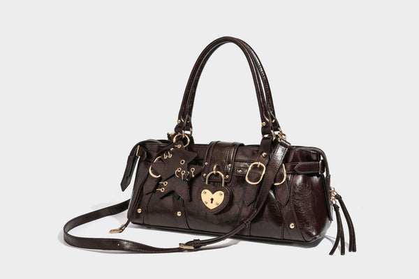 Glossy dark brown structured Boston satchel with heart-shaped lock charm, star pendant, rivet studs, multi-strap front panel