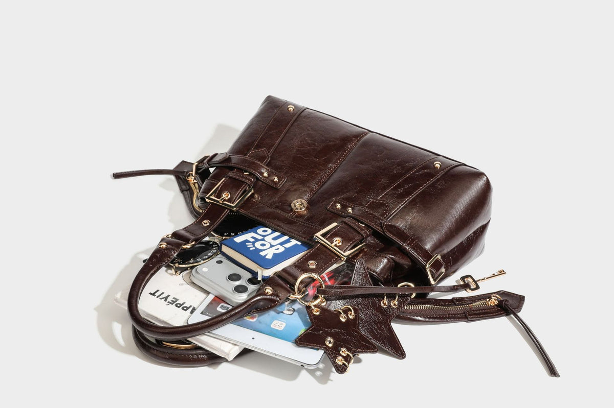 Structured leather-look satchel bag with heart padlock charm, star charm, gold-tone buckle hardware, dual top handles, and