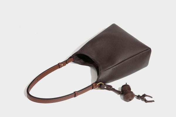 Hobo-Schultertasche in dunklem Espresso mit genarbter Oberfläche, warmen cognacfarbenen Details, verstellbarem schmalem Riemen, goldfarbenen Ringbeschlägen und geknotetem