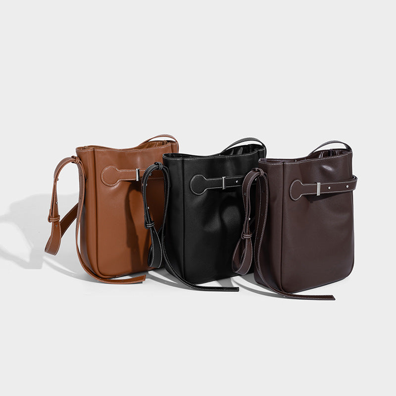 Structured dark brown leather-look bucket bag with white contrast stitching, front wraparound belt buckle strap, and long