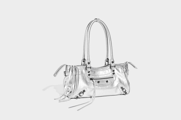 Längliche Schultertasche in Zylinderform mit glänzender Lederoptik, silberfarbenen Nietenbeschlägen, seitlichen Quasten und mehreren außenliegenden Reißverschlüssen
