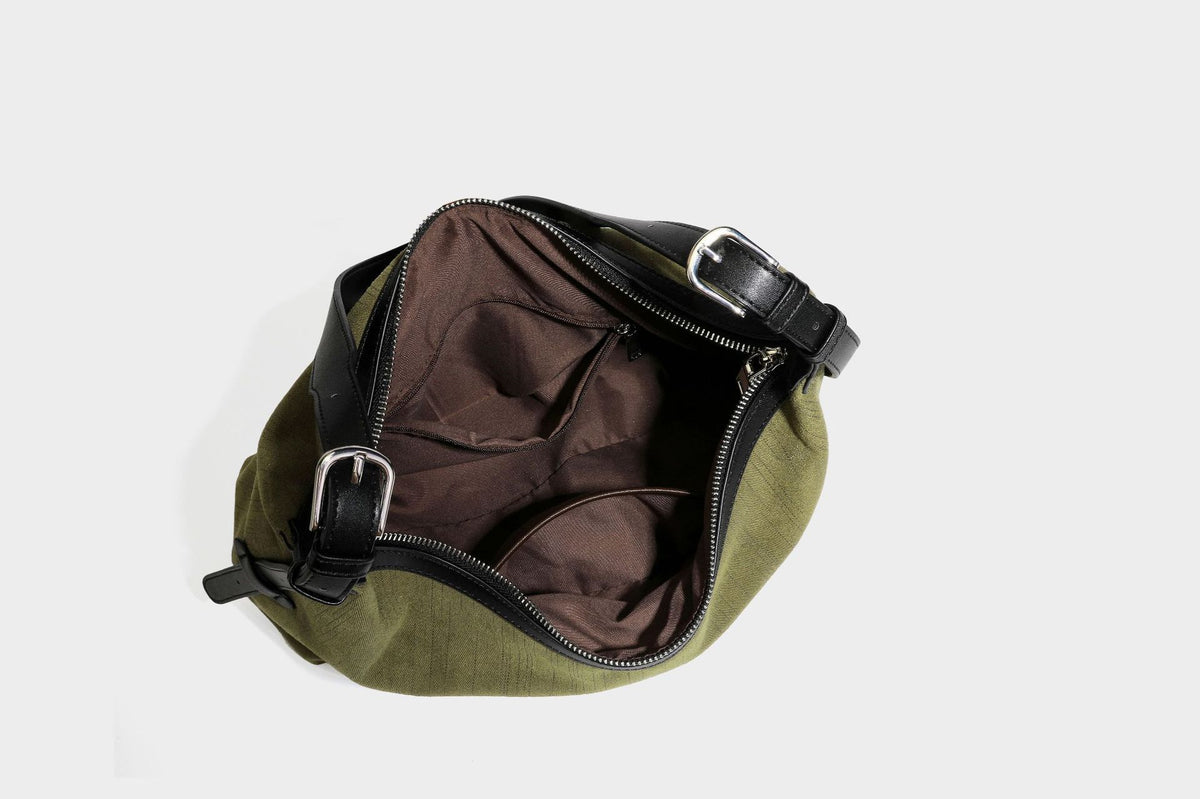 Slouchy olive green canvas hobo shoulder bag with black leather-look trim, zip-top closure, and adjustable strap, detail view