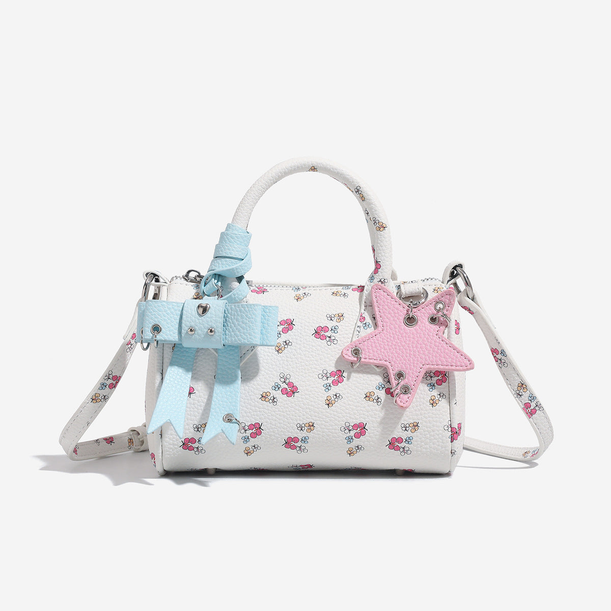 Weiße Mini-Boston-Handtasche mit genarbter Oberfläche und Blumen- oder Kirschprint, pastellblauem Schleifenanhänger, rosafarbenem Sternanhänger und zwei oberen Henkeln
