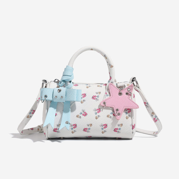 Weiße Mini-Boston-Handtasche mit genarbter Oberfläche und Blumen- oder Kirschprint, pastellblauem Schleifenanhänger, rosafarbenem Sternanhänger und zwei oberen Henkeln