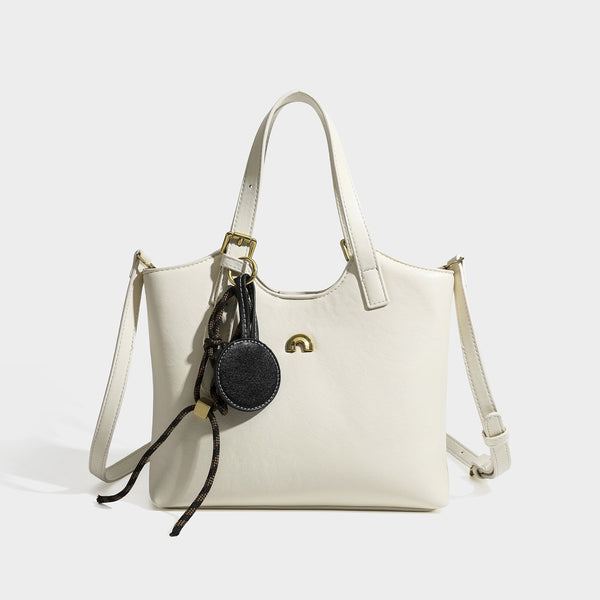 Structured smooth leather-look tote bag with long shoulder strap, gold-tone hardware, and hanging tassel-coin charm, detail