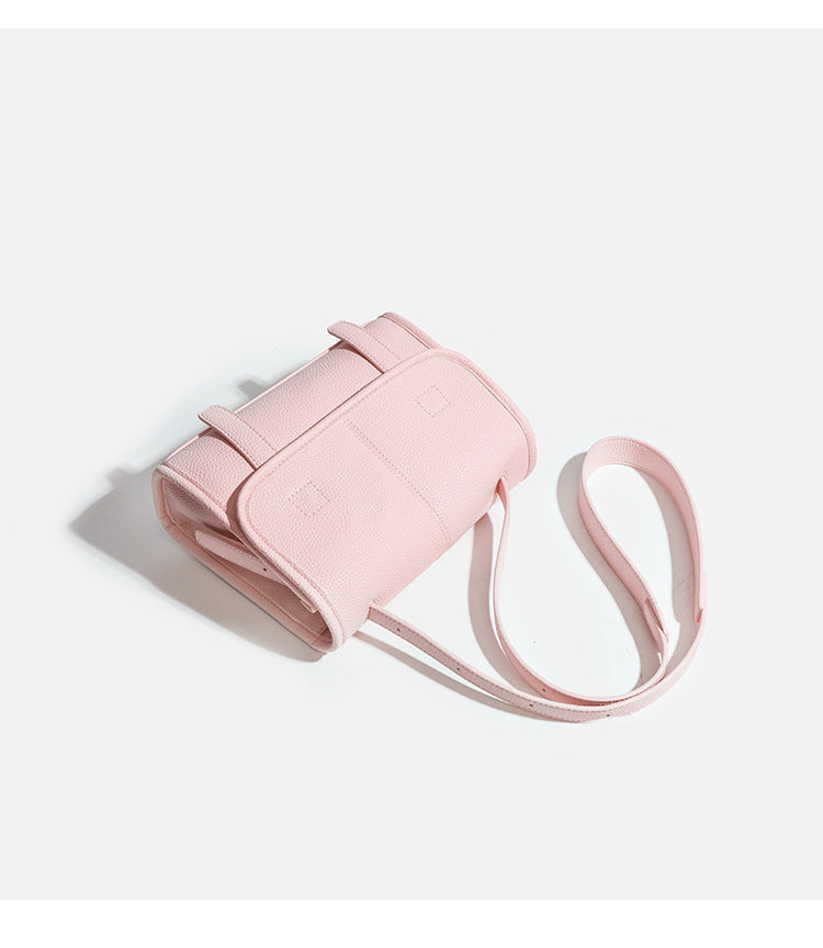 Compact structured flap satchel bag with pebbled texture, snap closure, front strap tabs, and long adjustable crossbody